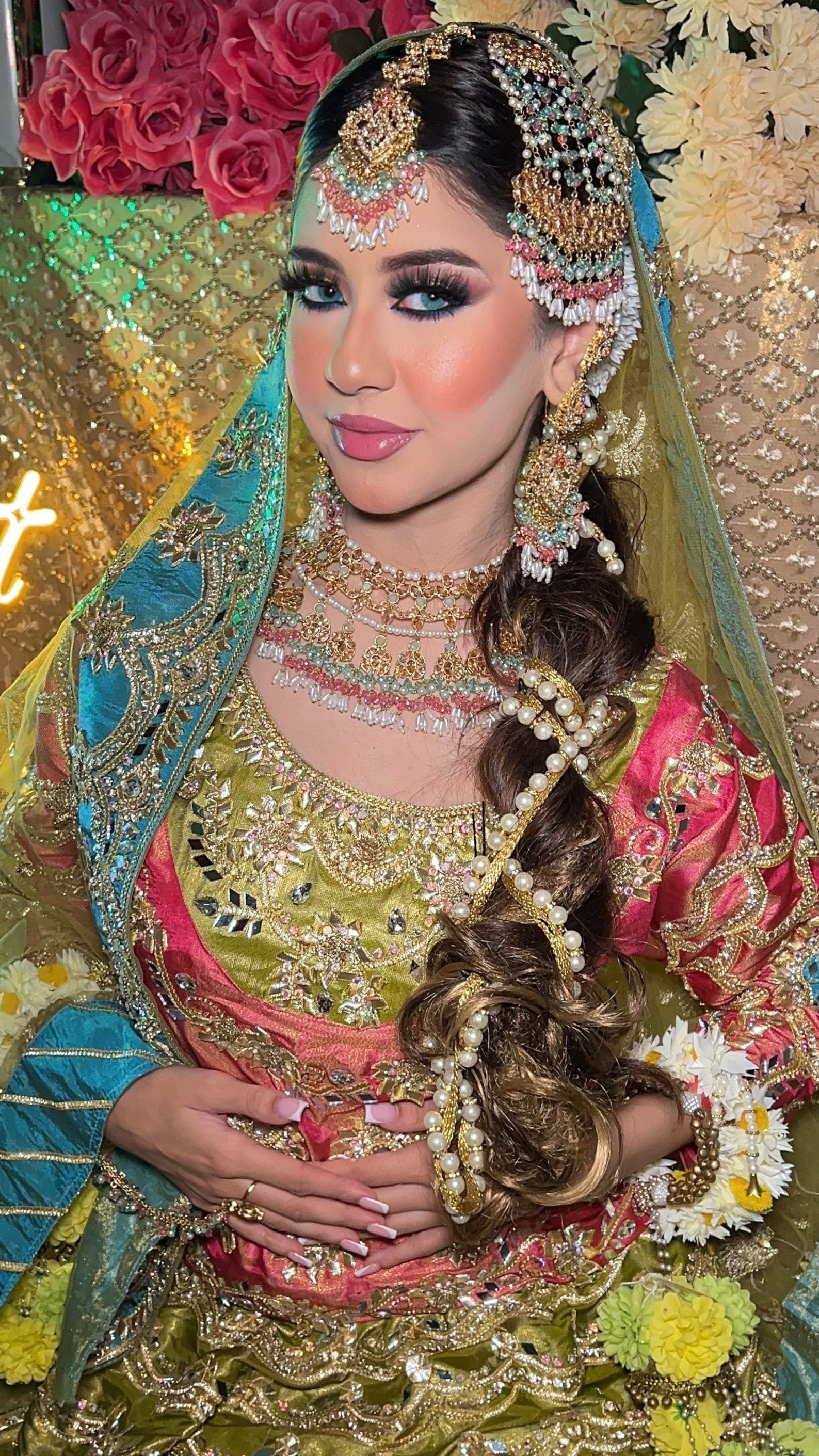 Woman in traditional bridal attire with intricate jewelry and makeup, set against a decorated background.